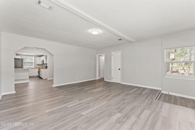 unfurnished living room with visible vents, baseboards, a textured ceiling, arched walkways, and light wood-style flooring