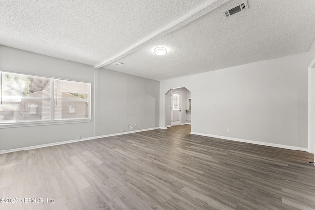 unfurnished living room featuring arched walkways, a textured ceiling, baseboards, wood finished floors, and visible vents