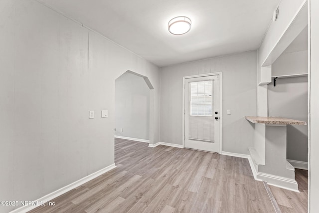 interior space featuring arched walkways, baseboards, and light wood-style flooring
