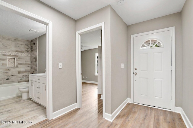 foyer entrance with baseboards, light wood finished floors, and visible vents