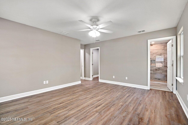 unfurnished bedroom with visible vents, connected bathroom, baseboards, and wood finished floors