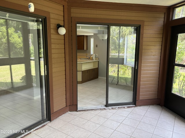 doorway to outside featuring light tile patterned floors, wood walls, a sink, and a healthy amount of sunlight