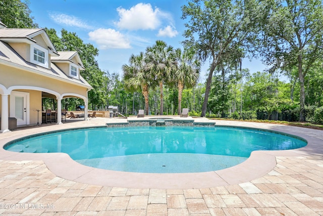 view of pool featuring a pool with connected hot tub, a patio area, and view of wooded area