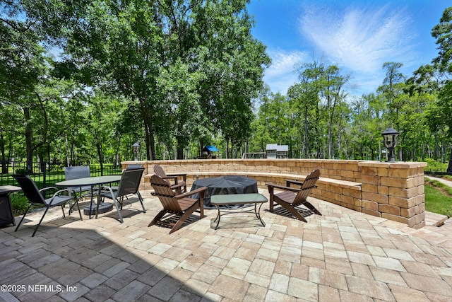 view of patio with fence, an outdoor fire pit, outdoor dining space, and view of wooded area