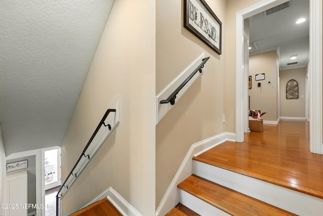 stairs featuring attic access, wood finished floors, baseboards, and a textured ceiling