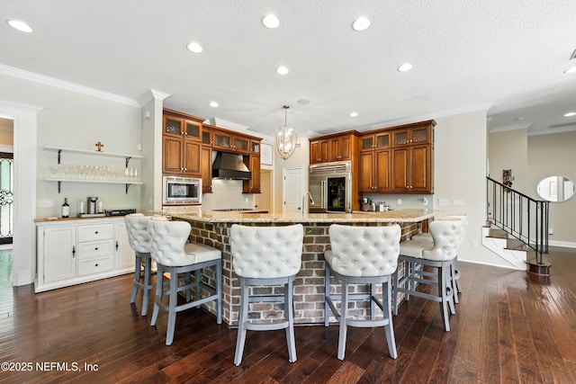kitchen with built in appliances, under cabinet range hood, brown cabinetry, crown molding, and glass insert cabinets