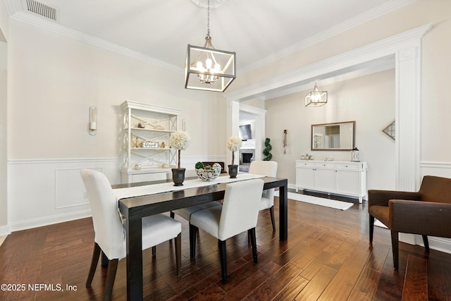 dining space with a chandelier, crown molding, dark wood-style floors, and wainscoting