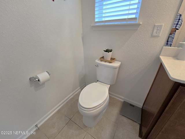 half bath featuring a textured wall, tile patterned flooring, vanity, toilet, and baseboards