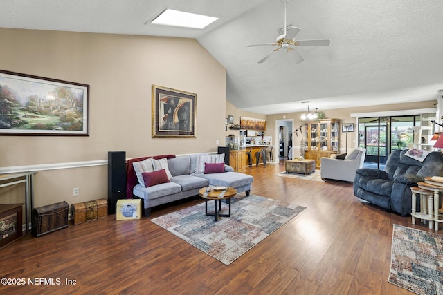 living area with ceiling fan with notable chandelier, wood finished floors, a skylight, and high vaulted ceiling