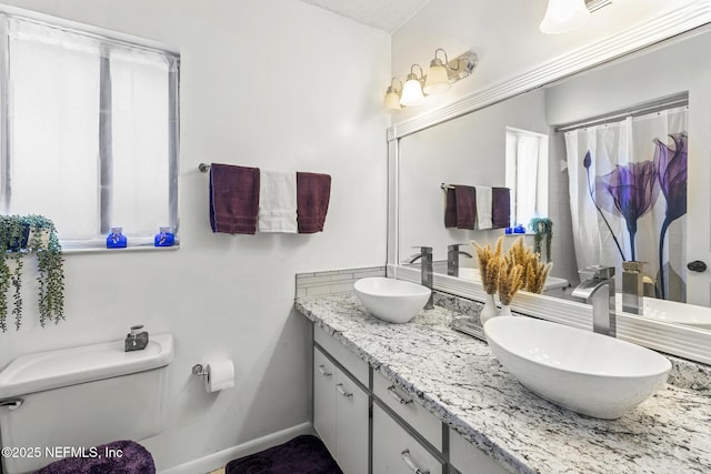 full bathroom featuring double vanity, a sink, baseboards, and toilet