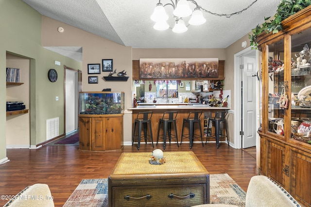 living room featuring bar, a textured ceiling, visible vents, wood finished floors, and an inviting chandelier
