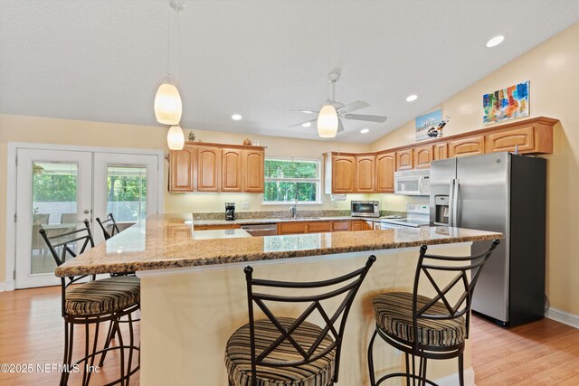 kitchen with stainless steel appliances, a sink, light wood finished floors, a breakfast bar, and lofted ceiling