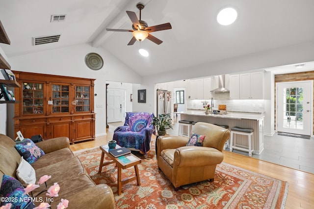 living room featuring beamed ceiling, light wood-type flooring, and visible vents