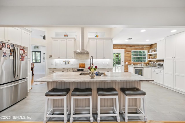 kitchen featuring stainless steel appliances, a healthy amount of sunlight, a kitchen breakfast bar, and wall chimney exhaust hood