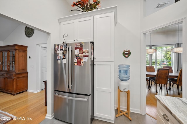kitchen with white cabinets, light stone counters, light wood finished floors, freestanding refrigerator, and baseboards