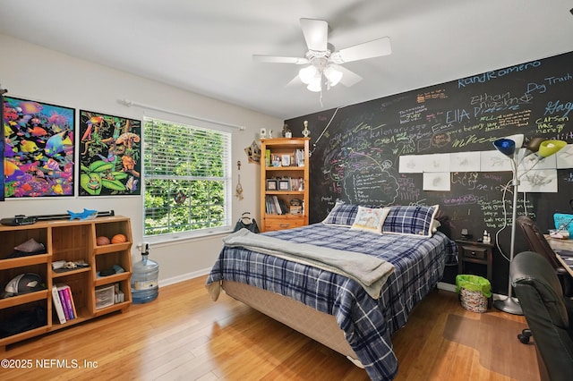 bedroom featuring baseboards, ceiling fan, wood finished floors, and an accent wall