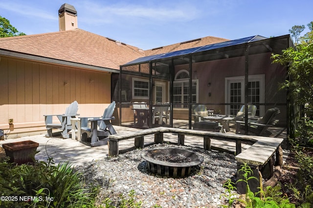 back of property with a lanai, a chimney, roof with shingles, an outdoor fire pit, and a patio