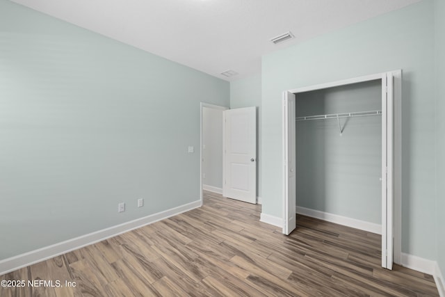 unfurnished bedroom featuring baseboards, visible vents, wood finished floors, and a closet