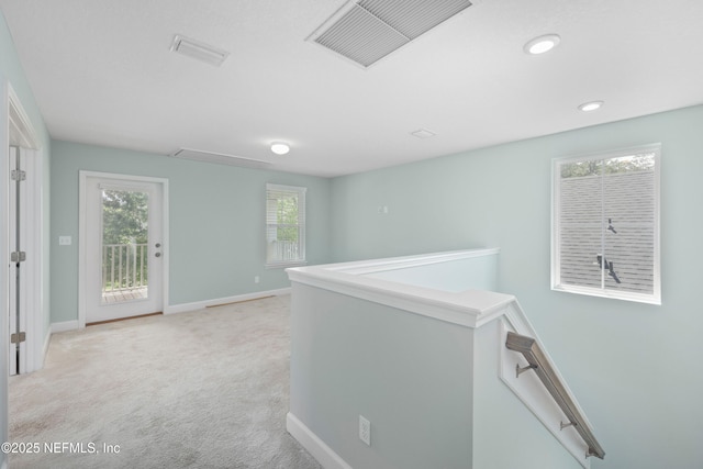 corridor with attic access, visible vents, light colored carpet, baseboards, and an upstairs landing