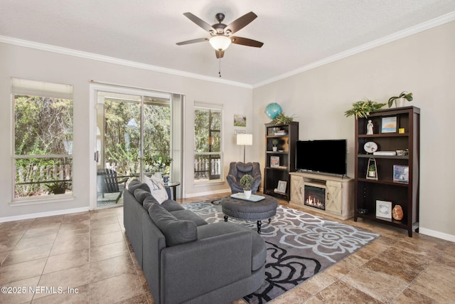 living room featuring healthy amount of natural light, ceiling fan, a lit fireplace, ornamental molding, and baseboards
