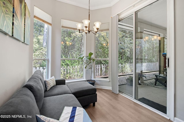 sunroom featuring wood finished floors, a chandelier, ornamental molding, and baseboards