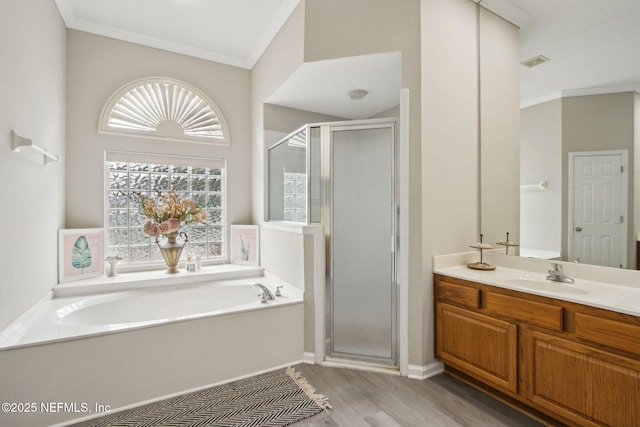 bathroom featuring ornamental molding, a stall shower, a garden tub, wood finished floors, and vanity