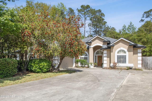 view of front of house with driveway, stucco siding, fence, and a garage