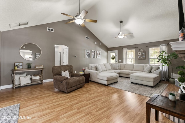 living room featuring ceiling fan, light wood-style floors, arched walkways, high vaulted ceiling, and visible vents