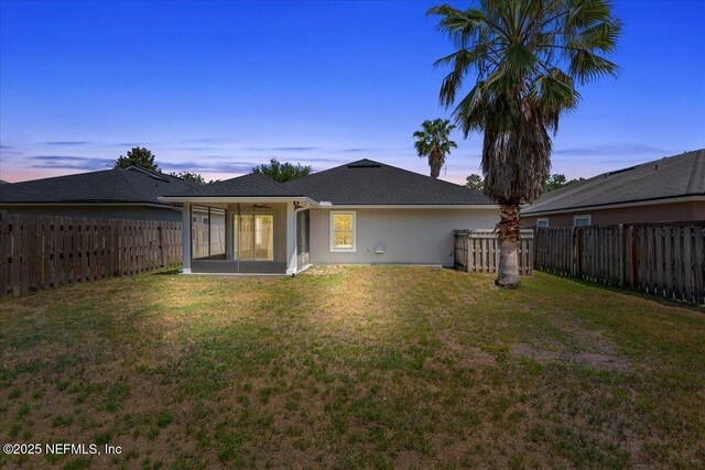 back of property featuring a fenced backyard, stucco siding, a sunroom, a ceiling fan, and a lawn