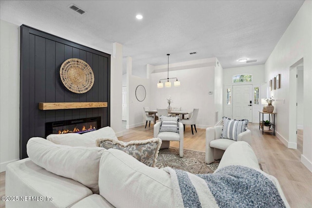 living room with visible vents, light wood-style flooring, baseboards, and a fireplace