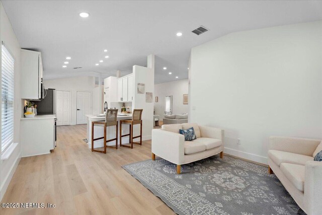 living room with visible vents, light wood-style floors, baseboards, and vaulted ceiling