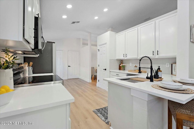 kitchen featuring visible vents, white cabinetry, a sink, a peninsula, and light wood-style flooring