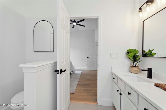 bathroom with vanity, wood finished floors, toilet, baseboards, and ceiling fan