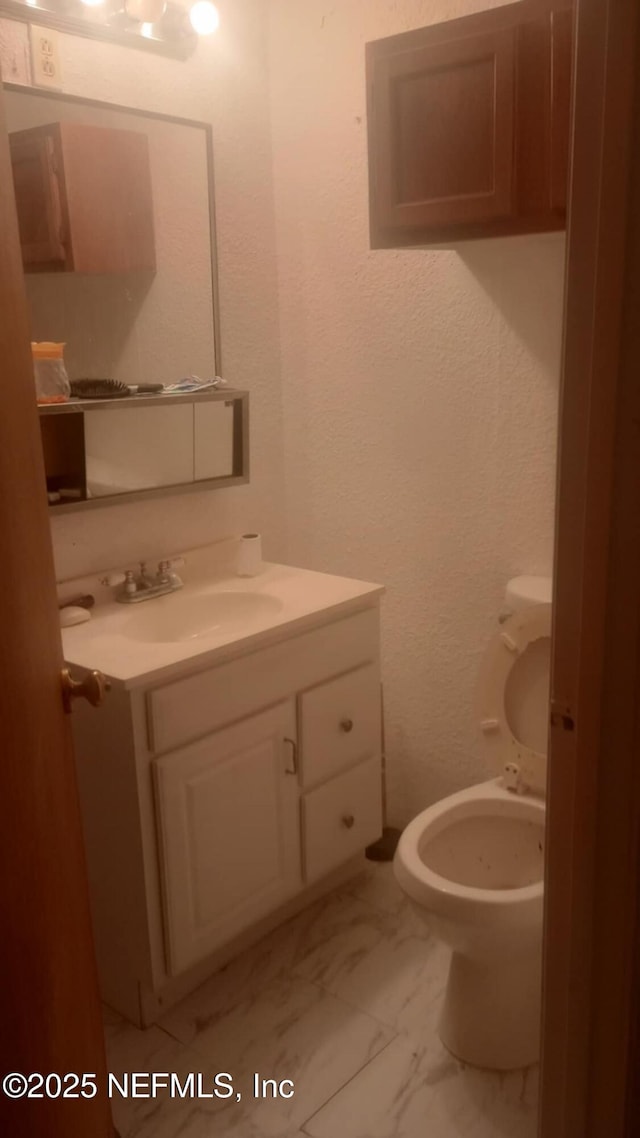 half bathroom featuring vanity, a textured wall, toilet, and marble finish floor