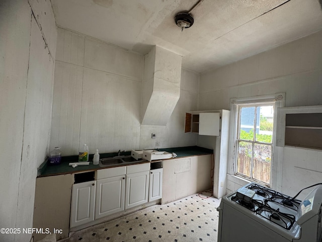 kitchen with dark countertops, light floors, white gas range, white cabinetry, and a sink
