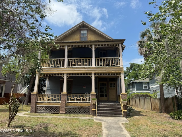 view of front facade featuring a porch, a front lawn, fence, and a balcony