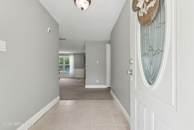 entryway with baseboards, a textured ceiling, light tile patterned flooring, and light carpet