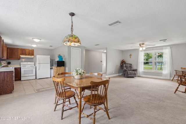 dining area with light colored carpet, a textured ceiling, visible vents, and ceiling fan