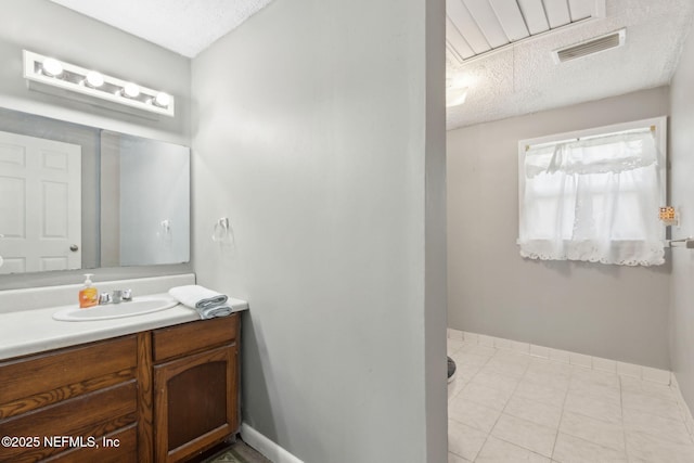 bathroom with visible vents, vanity, baseboards, a textured ceiling, and tile patterned floors