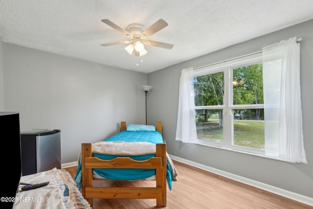 bedroom with baseboards, freestanding refrigerator, a textured ceiling, and wood finished floors