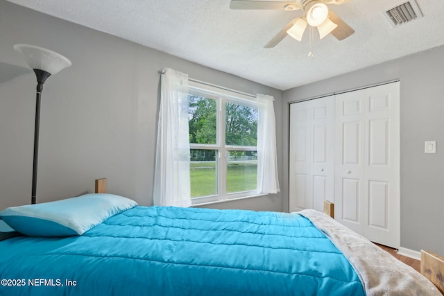 bedroom with a ceiling fan, a textured ceiling, visible vents, wood finished floors, and a closet