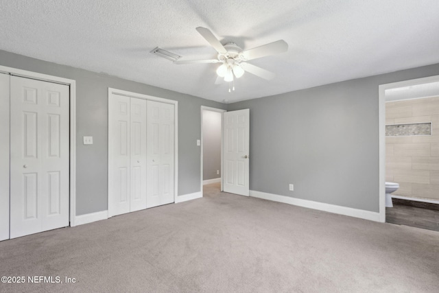 unfurnished bedroom featuring baseboards, ensuite bathroom, carpet, and two closets