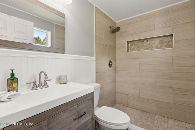 full bath featuring vanity, wainscoting, toilet, and tiled shower