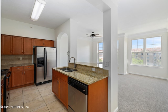 kitchen with a sink, arched walkways, brown cabinetry, stainless steel appliances, and a ceiling fan