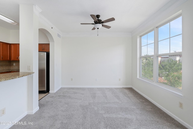 unfurnished living room featuring visible vents, ornamental molding, light colored carpet, arched walkways, and a ceiling fan