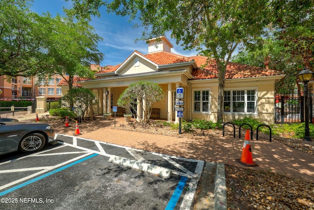 view of front of house with uncovered parking, fence, covered porch, stucco siding, and a tile roof