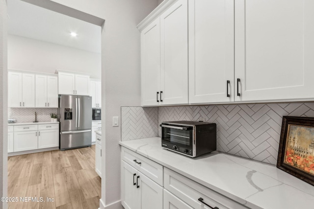 36039 Pitch Ln, Hilliard, FL 32046 - kitchen with stainless steel fridge with ice dispenser, backsplash, white cabinetry, and light stone countertops