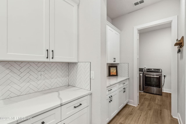 36039 Pitch Ln, Hilliard, FL 32046 - kitchen featuring washer and clothes dryer, white cabinetry, backsplash, light wood-style flooring, and light stone countertops