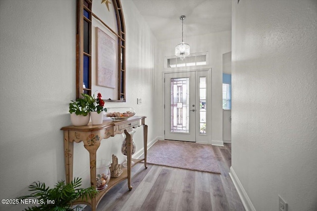 entryway featuring an inviting chandelier, baseboards, a textured wall, and wood finished floors