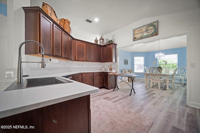 kitchen featuring an inviting chandelier, a sink, light countertops, lofted ceiling, and light wood-type flooring